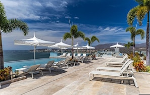 A poolside area with lounge chairs and umbrellas, overlooking a body of water and mountains. - 4-bed Beachfront Lux Apartment (Bucerías)