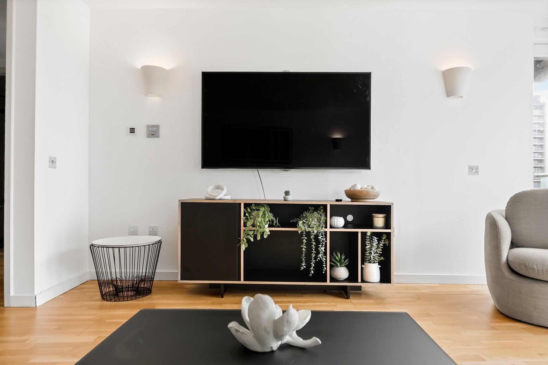 Un salon moderne avec un meuble de rangement noir pour l’équipement audiovisuel, un téléviseur à écran plat et un canapé gris.