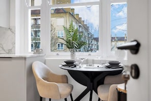 Ein Essbereich mit einem Tisch für zwei Personen, einem Topfpflanzen und Blick auf Gebäude durch ein Fenster.