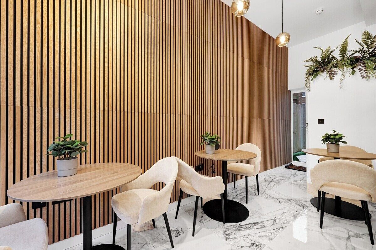 Ein modernes Interieur mit Holzlamellen, Marmorböden und runden Tischen mit Stühlen.