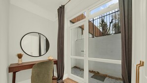 A room with a wooden desk, a round mirror, a green chair, a sliding glass door, and a view of the outside. - Large Stylish 2 Bed Flat near Kensington (London)