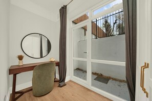 Habitació amb escriptori de fusta, un mirall rodó, una cadira verda, una porta corredissa de vidre i vista cap a l'exterior.