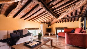 A spacious living area with a wooden ceiling, a sofa, a red armchair, a coffee table, and a television. - Deluxe View Apartment in Borgo di Matraia (Capannori)