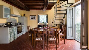A kitchen with a dining area, wooden ceiling beams, a staircase, and a sliding glass door leading to an outdoor area. - Deluxe View Apartment in Borgo di Matraia (Capannori)