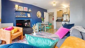 Een woonkamer met een bank, een televisie, een open haard en een eethoek met stoelen.