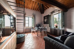 A spacious room with a wooden ceiling, a dining area with a table and chairs, a grey sofa, and large windows with curtains. - Superior Garden Borgo di Matraia (Capannori)