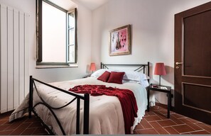 A bedroom with a bed, a window, a door, a nightstand, a lamp, and a framed picture on the wall. - Superior Garden Borgo di Matraia (Capannori)