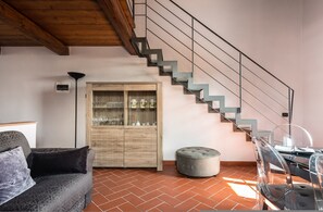 A modern interior with a wooden staircase, a sofa, a cabinet with glass doors, and a dining area. - Superior Garden Borgo di Matraia (Capannori)
