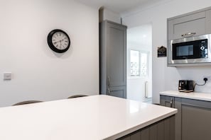 A modern kitchen with a white countertop, a wall-mounted clock, a microwave, and a coffee maker.