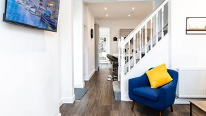A modern interior with a blue armchair, a staircase, and a framed picture on the wall. - 1-min Walk to High St 3-min to Mumbles Beach (Swansea)