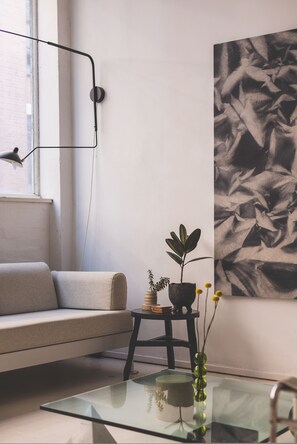 A modern living room with a sofa, a glass coffee table, a small side table with a plant, and a large abstract painting on the wall. - Modern Flat in the Heart of Bethnal Green (London)