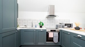 Een moderne keuken met blauwgroene kastjes, witte tegels, een roestvrijstalen afzuigkap, een magnetron en een vaatwasser.