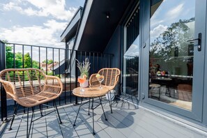 A balcony with wicker chairs and a small table, a potted plant, and a glass door leading to an outdoor area. - Omega Acton Top Floor (London)