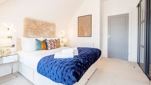 Een moderne slaapkamer met een groot bed, een zacht hoofdbord en een decoratief wandobject.
