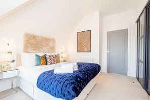 A modern bedroom with a large bed, a fluffy headboard, and a decorative wall piece. - Omega Acton Top Floor (London)