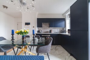 A modern kitchen with dark cabinets, a glass dining table, and a chandelier. - Spacious Modern 3 Beds 3 Baths in Finchley (London)