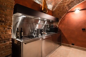 A modern kitchen with stainless steel appliances, a brick wall, and a hanging light fixture. - Masaccio Apartament in Villa Guinigi (Capannori)