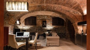 Una stanza con soffitto a volta in mattoni, una scrivania con un computer, un divano e una televisione.
