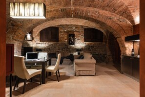 A room with an arched brick ceiling, a desk with a computer, a sofa, and a television. - Masaccio Apartament in Villa Guinigi (Capannori)