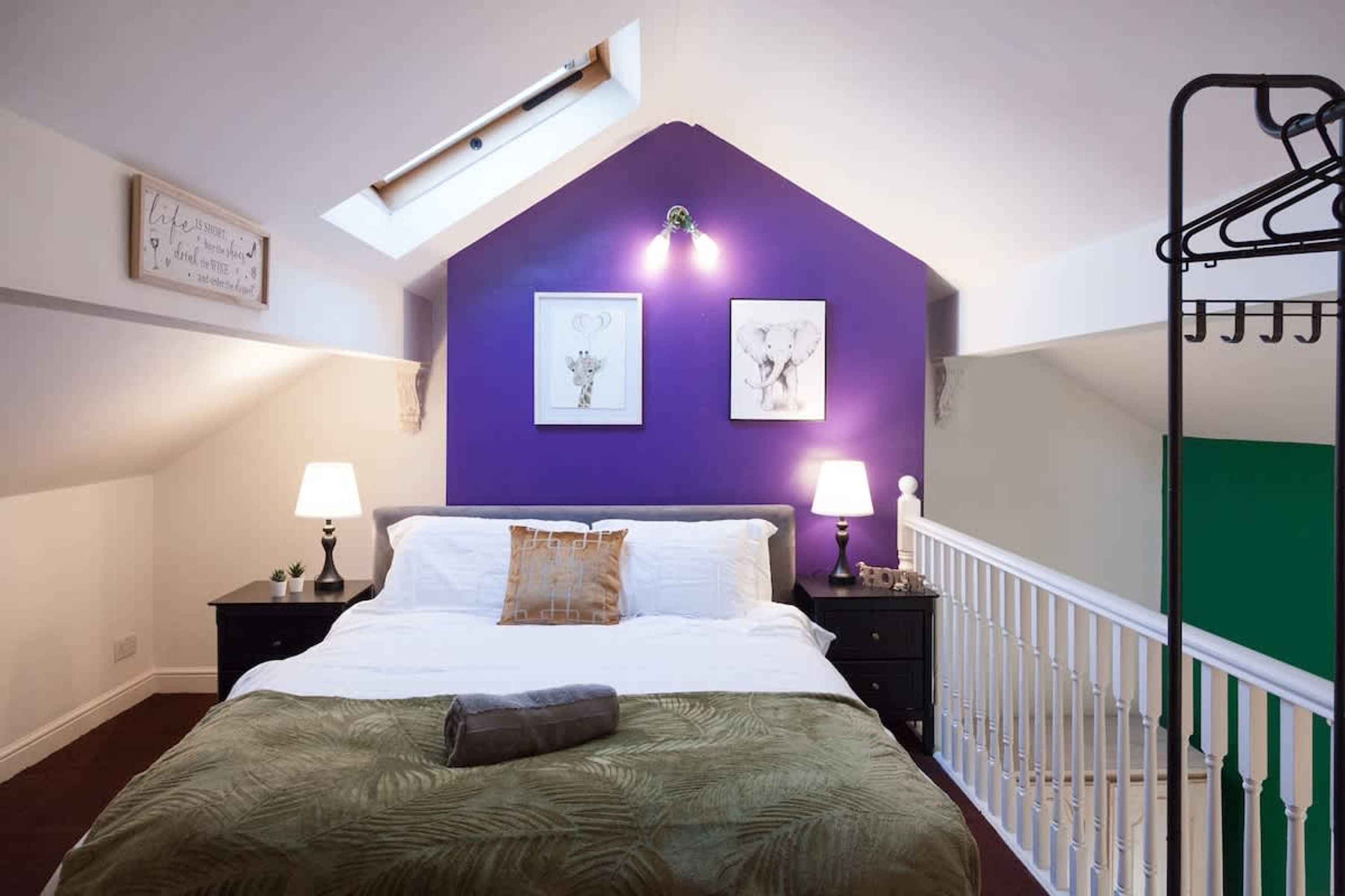 Une chambre avec un plafond en pente, un lit recouvert d’une couverture verte, deux tables de chevet avec des lampes et une étagère fixée au mur.