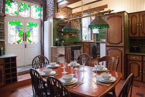 Un comedor con una mesa de madera dispuesta para seis personas, rodeada de sillas, y una cocina al fondo.
