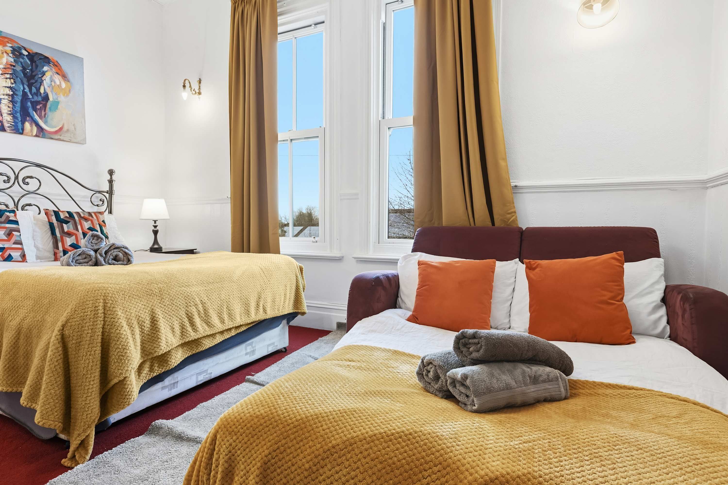 Une chambre d’hôtel avec deux lits, une fenêtre avec des rideaux, un tableau au mur et une lampe.