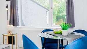 Quarto moderno com mesa de vidro redonda, cadeiras azuis, um globo em uma mesinha e vista para o verde lá fora.