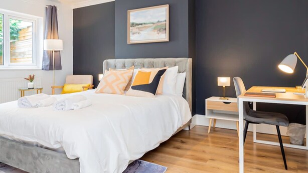 Quarto moderno com cama, mesas de cabeceira, escrivaninha e uma cadeira.