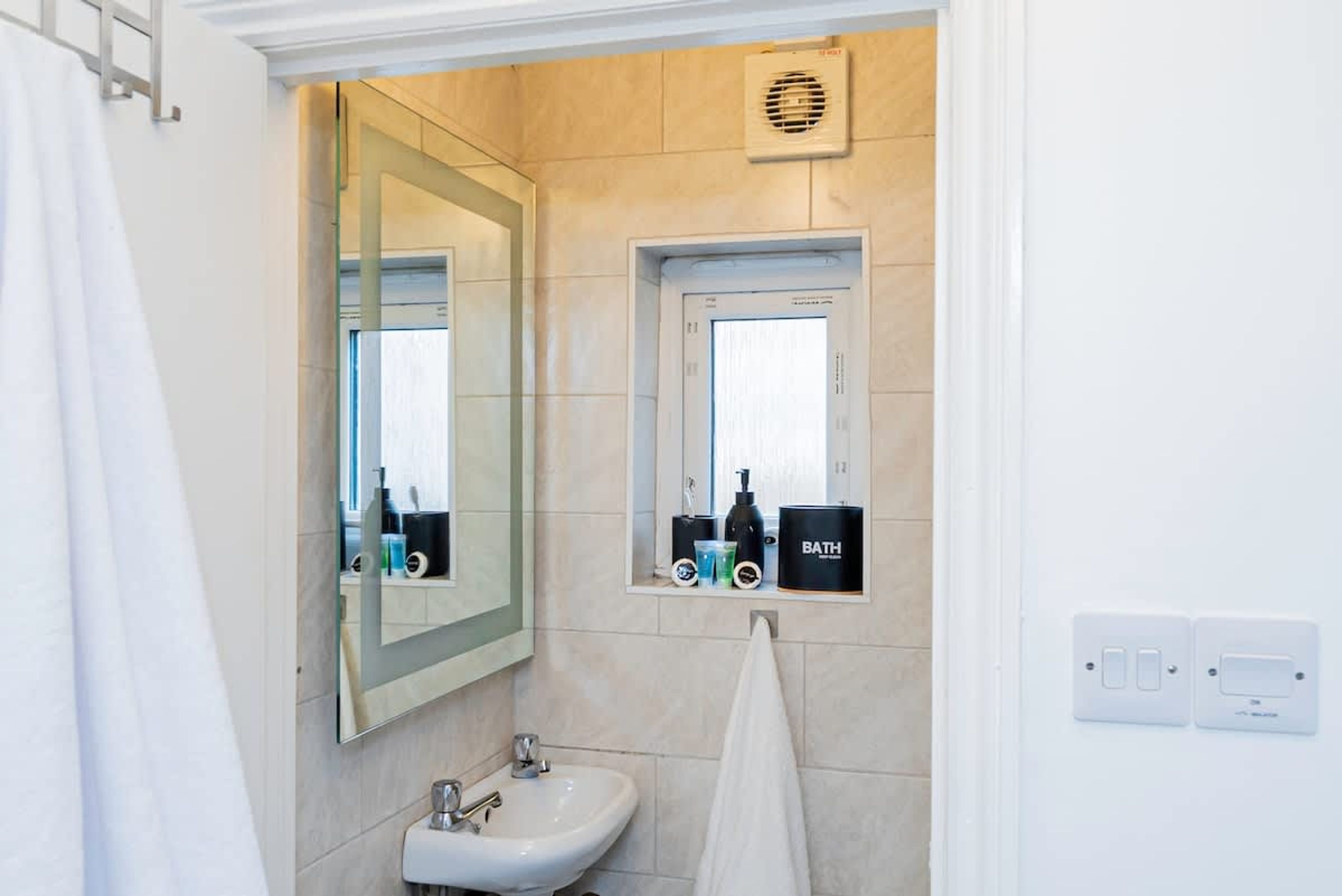 Une salle de bain équipée d’un lavabo, d’un miroir, d’un porte-serviettes et d’une petite fenêtre, ainsi que de produits de toilette.