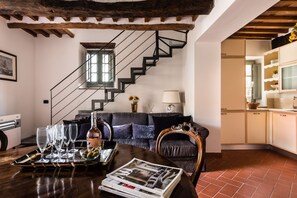 Ein Wohnzimmer mit Sofa, einem Esstisch mit Gläsern und einer Flasche, einer Treppe und einem Küchenbereich.