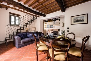 Ein Wohnzimmer mit einer Couch, Stühlen, einem Esstisch, einer Treppe und einer Küchenzeile.