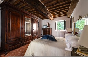 Ein Schlafzimmer mit großem Holzschrank, einem Bett mit weißer Bettwäsche und einem Fenster mit Blick auf Grünflächen.