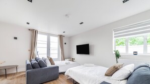 Ein modernes Hotelzimmer mit einer Couch, zwei Betten, einem Fernseher und einem Fenster mit Vorhängen.
