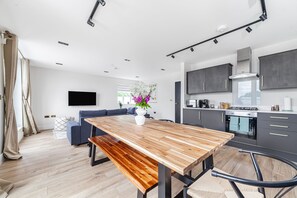 A modern kitchen with dark cabinets, a wooden dining table, and a built-in oven. - Stunning Penthouse in the Heart of Wembley (Wembley)