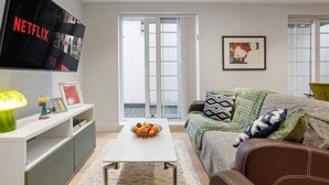 En stue med et fladskærms-tv, et sofabord med frugt, en sofa med mønstrede puder og en skydedør i glas.