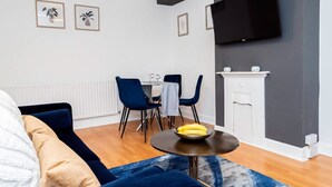 Una sala de estar moderna con un sofá, una mesa de comedor con sillas, un televisor de pantalla plana en la pared y una chimenea.