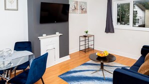 Una sala moderna con televisión, chimenea, mesa de comedor y sillas azules.