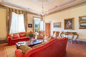 A spacious living room with a red sofa, patterned armchairs, a coffee table, and a chandelier. - Villa di Buona Speranza - Oasis of Serenity (Lucca)