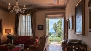 A room with a red sofa, patterned armchairs, a chandelier, and a view through an open door. - Villa di Buona Speranza - Oasis of Serenity (Lucca)