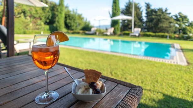 A glass of amber-colored beverage with a garnish, a bowl of ice cream with a cherry, and a pool in the background. - Villa di Buona Speranza - Oasis of Serenity (Lucca)