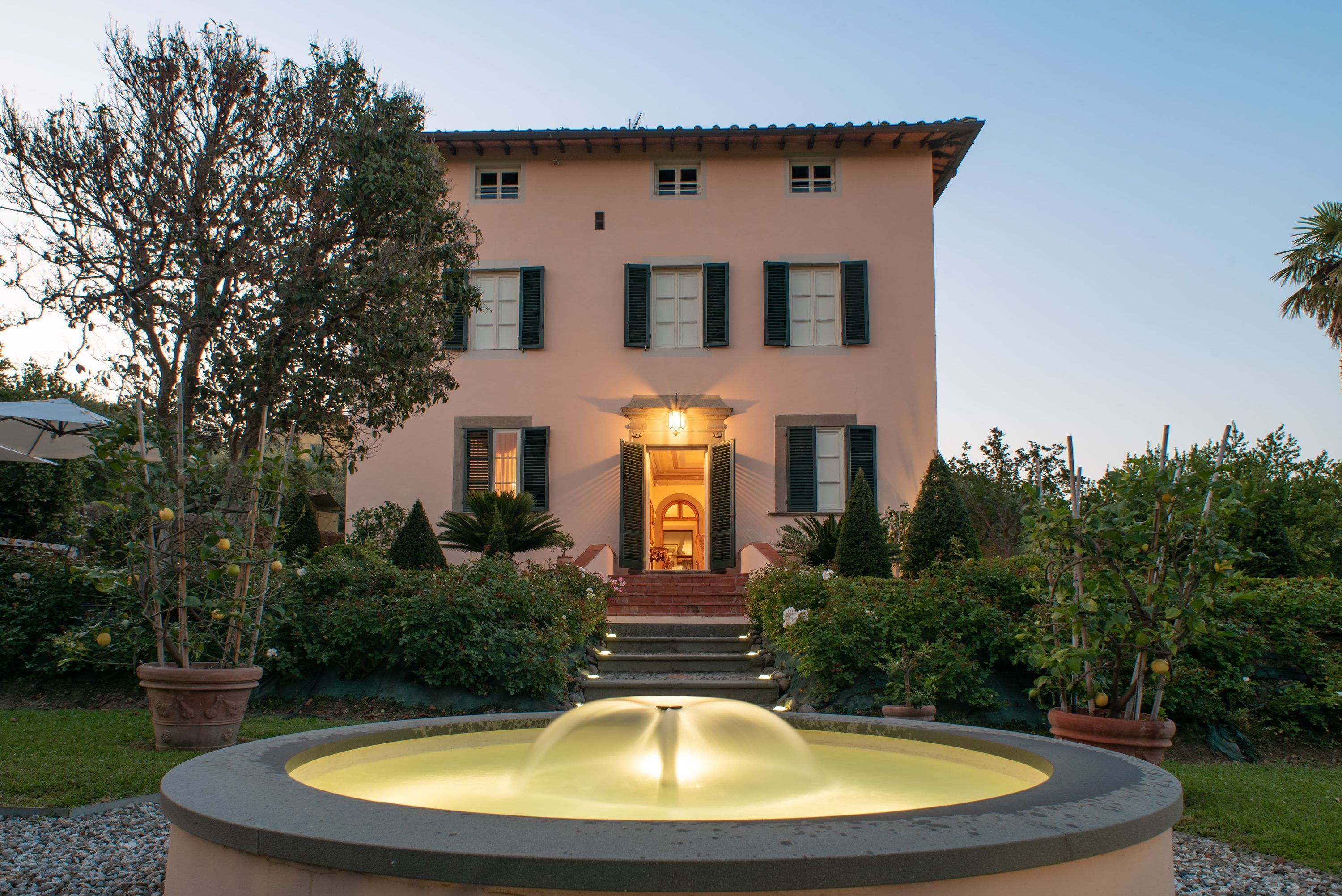 A building with a fountain in front, surrounded by potted plants and a well-kept garden.