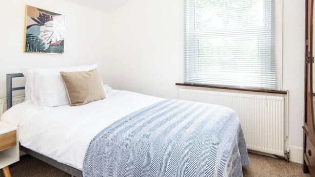 Un dormitorio con cama, ventana con persianas, radiador y armario de madera.