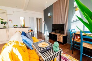 Ein modernes Wohnzimmer mit Sofa, Couchtisch, Fernseher und einem Essbereich mit Stühlen und Tisch.