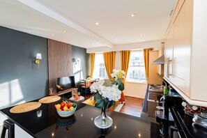 A modern kitchen with a central island, a dining area with a table and chairs, and a view of the city through large windows. - Stylish 2BR Near Hyde Park Museums Kensington (London)