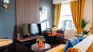 Un soggiorno moderno con una TV a schermo piatto, un tavolino rotondo, un divano e un'area pranzo con sedie.