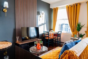 Ein modernes Wohnzimmer mit Flachbildfernseher, rundem Couchtisch, Sofa und Essbereich mit Stühlen.