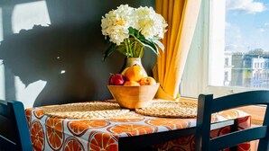 Un tavolo con una ciotola di frutta e fiori, una sedia e una finestra vista.