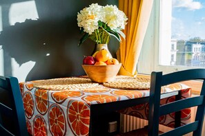Ein Tisch mit Obstschale und Blumen, ein Stuhl und ein Fenster mit Blick.