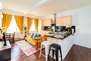 A modern kitchen with wooden cabinets, a central island, and a dining area with a sofa and chairs. - Stylish 2BR Near Hyde Park Museums Kensington (London)