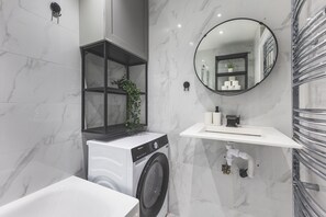 Ein modernes Badezimmer mit Waschmaschine, Waschbecken, Spiegel und Handtuchhalter.
